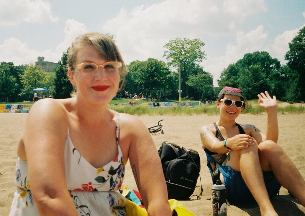 Sophie and Erin sitting in the sand and smiling, probably at Kat's beach birthday.