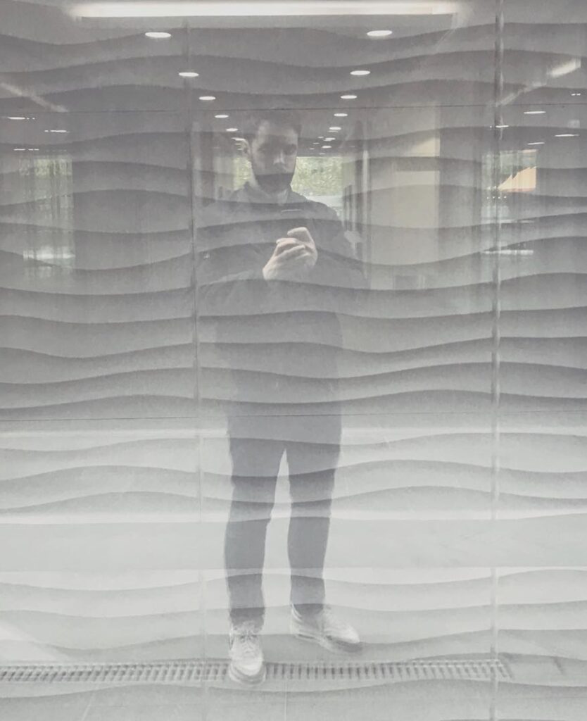 Will's reflection in a glass wall with wavy bands behind it