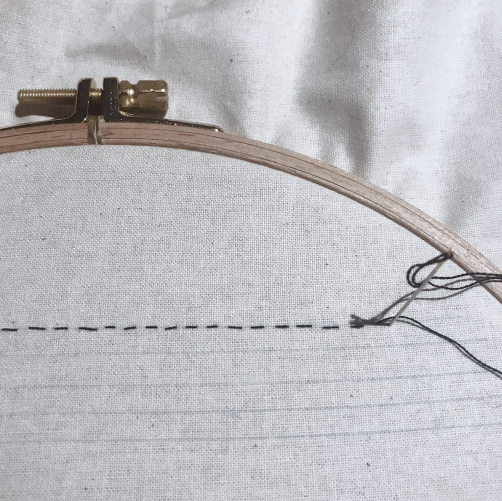 Will's embroidery hoop, with one running stitch along the top of a linear stencil.