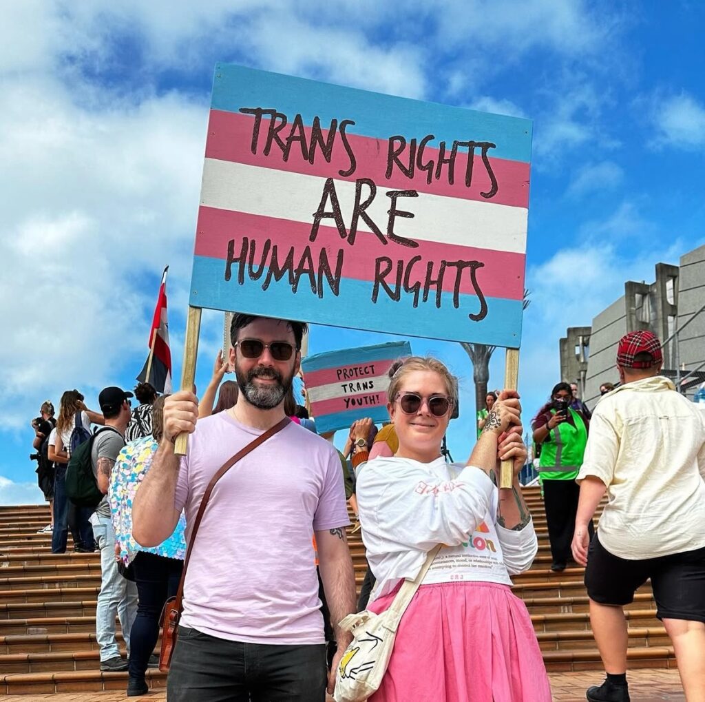 Will and Vee, holding a "trans rights are human rights" sign together.