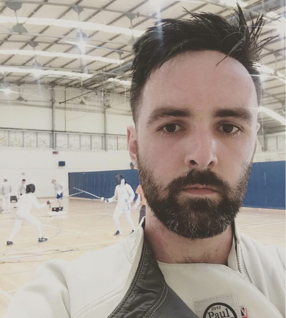 Will in fencing gear, in front of fencers